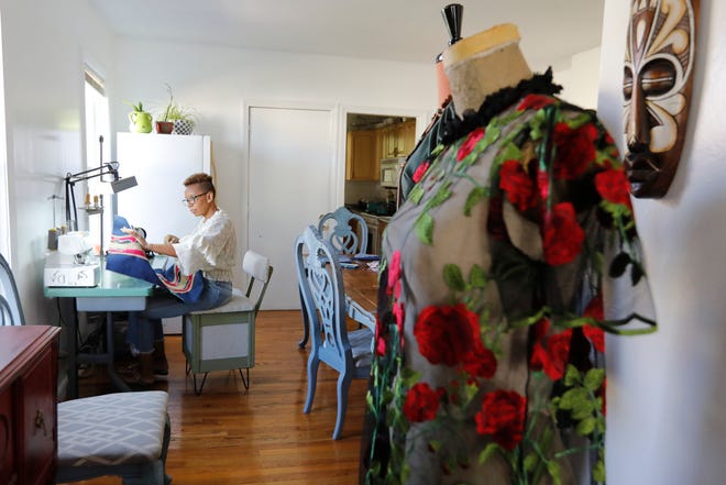 In the foreground is a dress created by Aidil Timas-Grogan, who is working on her latest designs at her home in New Bedford.