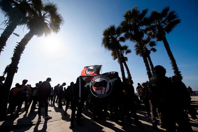 Counter-protesters, some carrying ANTIFA flags, stand under palm trees on the beach as they wait to confront protesters for a "patriot march" protest in support of US President Donald Trump on January 9, 2021, in the Pacific Beach neighborhood of San Diego, California.