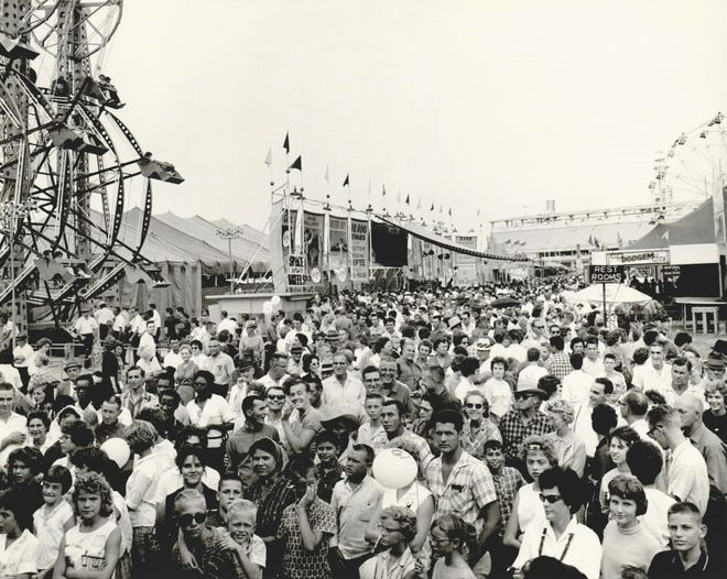 Standing shoulder to shoulder, a crowd of fairgoers navigate the Midway on Sept. 23, 1962, at the Oklahoma State Fair. The packed Midway included a new ride, the "Sky Wheel," a double Ferris wheel seen at left. The 55th state fair, themed "Man, Space and Progress," also featured a "Moon Base" exhibit, the "Chuting Stars" U.S. Navy precision parachute exhibition team and a public showing of the X-15 rocket-powered aircraft. This photo was published in the Oklahoma City Times.