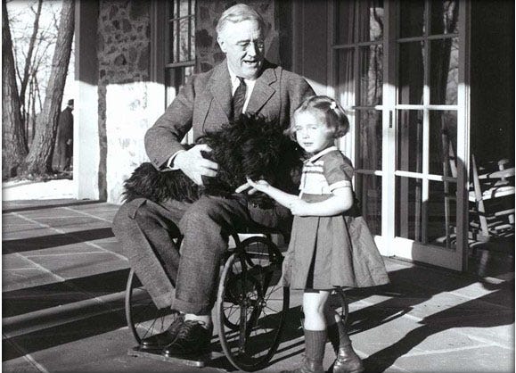 A rare photo of President Franklin D. Roosevelt in his wheelchair as he holds his dog Fala and talks to the daughter of Top Cottage's caretakers in Hyde Park in 1941.