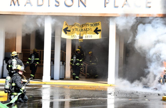 Firefighters enter an office building behind the burning vehicle at Madison Place shopping center Saturday.