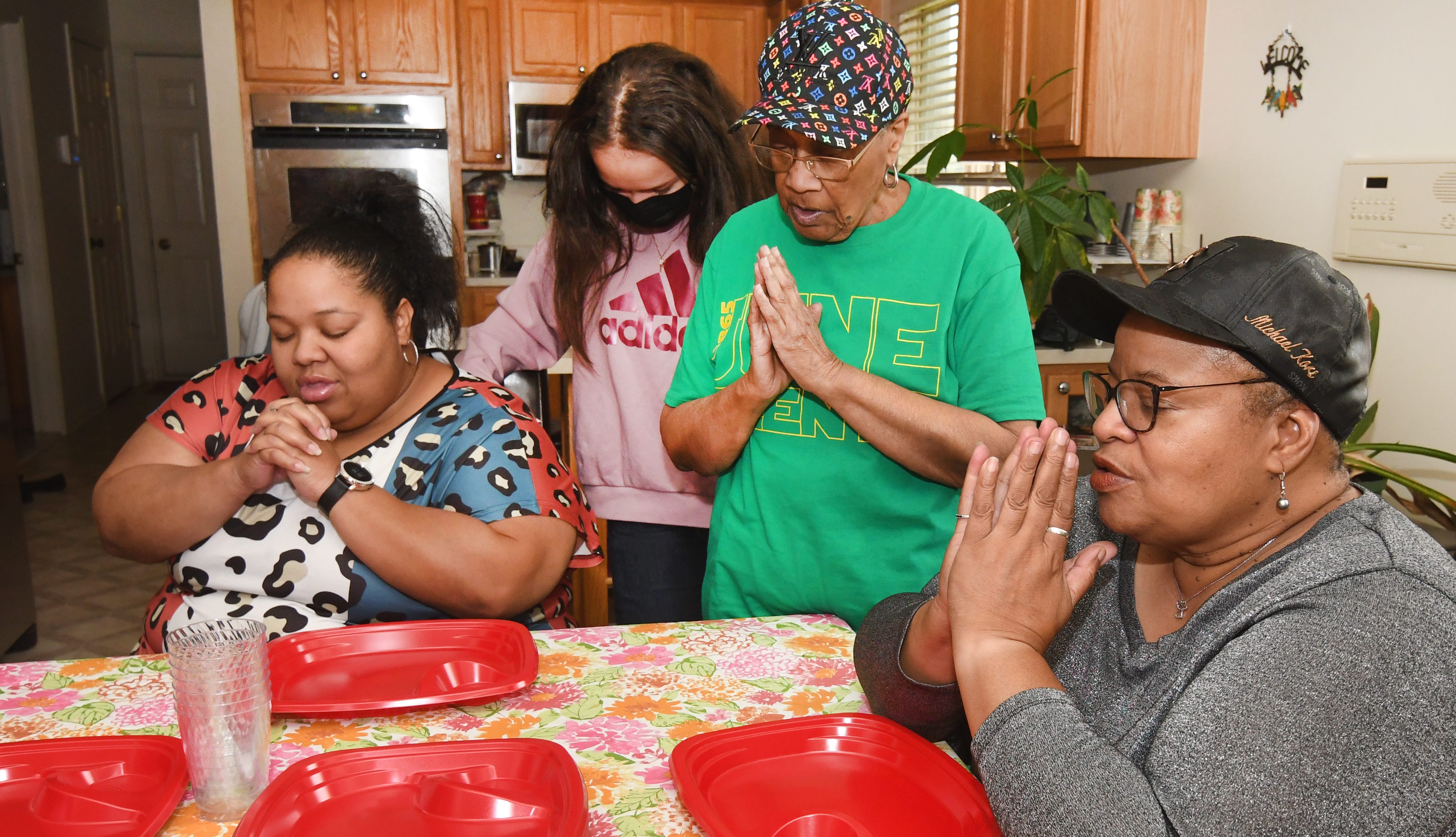 Neica Williams, from left, Selina Smith’s daughter, Chiara Smith, Selina Smith’s granddaughter, Delois McMillan, Selina Smith’s mother and Selina Smith as they pray before eating dinner at their Pontiac home. Selina Smith is a sandwiched generational caregiver.