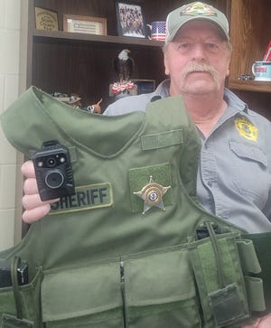 Scott County, Arkansas Sheriff Randy Shores holds a protective vest with a body camera in this photo.