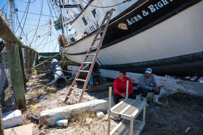 Shrimping boat workers Javier Allan Lopez, left, 34, and Oriel Martinez Alvarado, 51, sit in the shade of one of the shrimp boats that some of their fellow workers sought shelter in during Hurricane Ian on Wednesday afternoon near Trico Shrimp Company in Fort Myers, Fla., on Friday, September 30, 2022. With nowhere else to go, Alvarado said the workers resorted to moving from boat to boat as the storm made each successive vessel increasingly perilous.