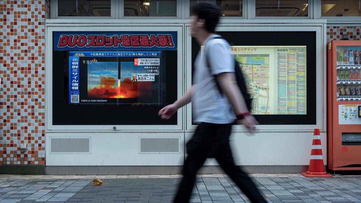 A man walks past a public television screen in Tokyo on October 4, 2022, displaying file missile footage during a broadcast about an early morning North Korean missile launch which prompted an evacuation alert over northeastern Japan.