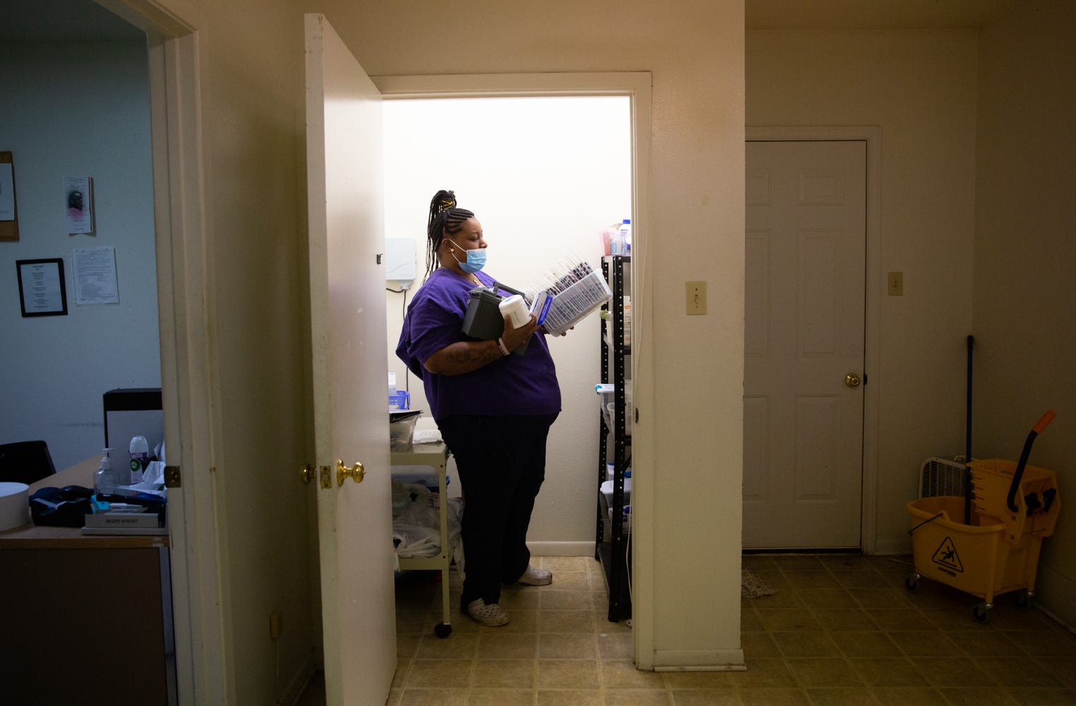 Tre'Asia Anderson gets her clients' medication out of hte locked closet where it is kept; her arms are full. The camera captures her from a doorway.
