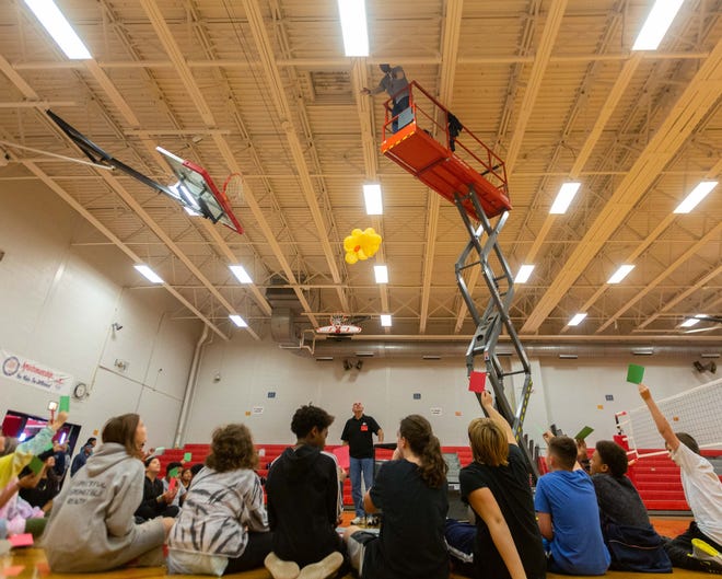 A Landon Middle School custodian drops a sixth-grade contraption, consisting of a cluster of balloons, as part of the school's annual egg drop competition.