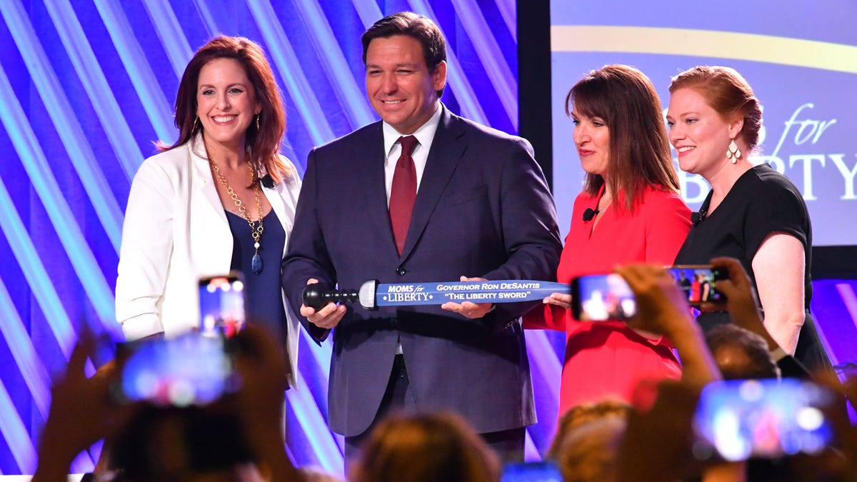 Florida Governor Ron Desantis, center, is presented "The Sword of Liberty" by Moms for Liberty co-founders Tiffany Justice, left, Tina Descovich, second from right and executive director of program outreach Marie Rogerson, far right, during the first Moms for Liberty National Summit on Thursday, July 15, 2022 in Tampa, Fla.