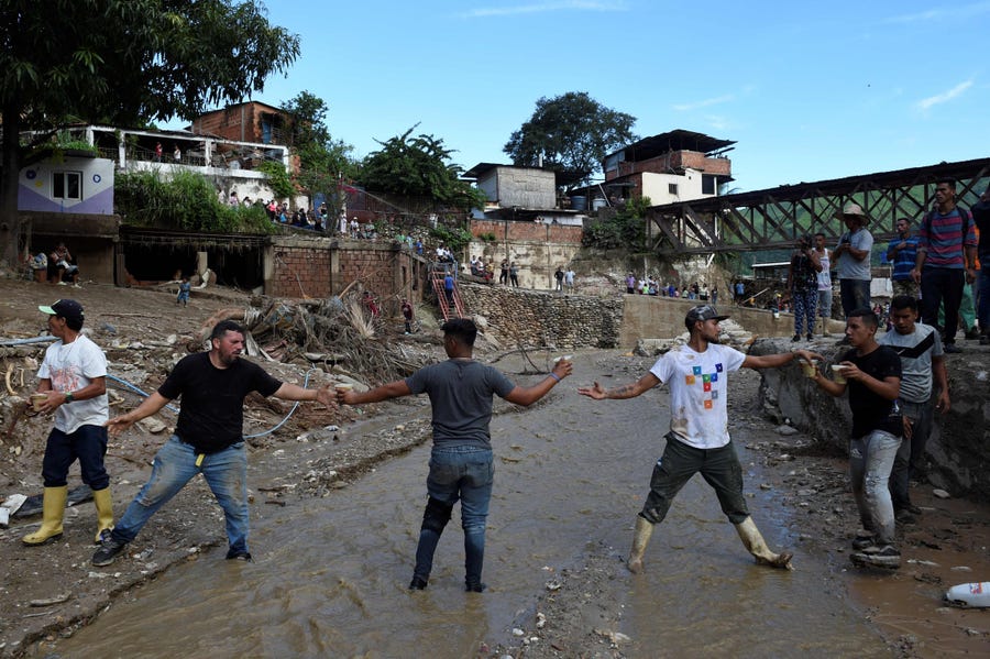 Residents make a human chain to deliver food to those affected by the landslide in Las Tejerias, Aguara state, Venezuela, on Oct.10, 2022. - At least 25 people died, and more than 50 are still missing after a river overflow caused a landslide in the latest deadly disaster to hit the country.