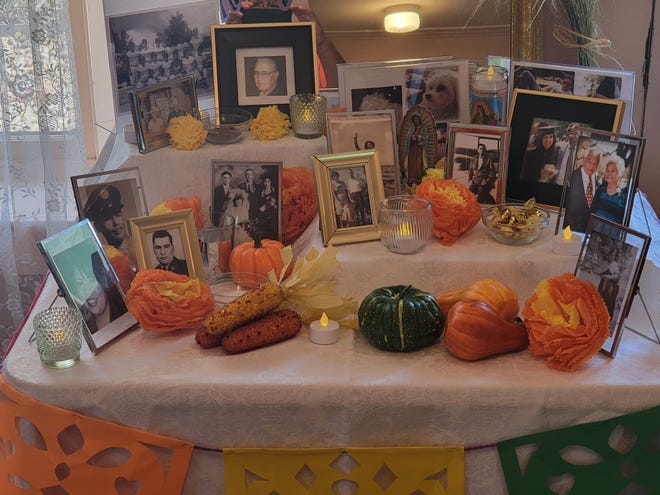 Family photos, food, candles and decorations line a Dios de los Muertos altar.