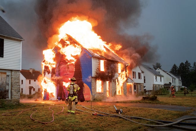 Artist Mandi Caskey’s performance piece “Seeds Sown in Fire” burns as firefighters monitor the blaze. Caskey painted her sister and niece on the sides of two abandoned homes before the Whitehall Division of Fire used one for a controlled burn. “The fire becomes the artist,” Caskey says.