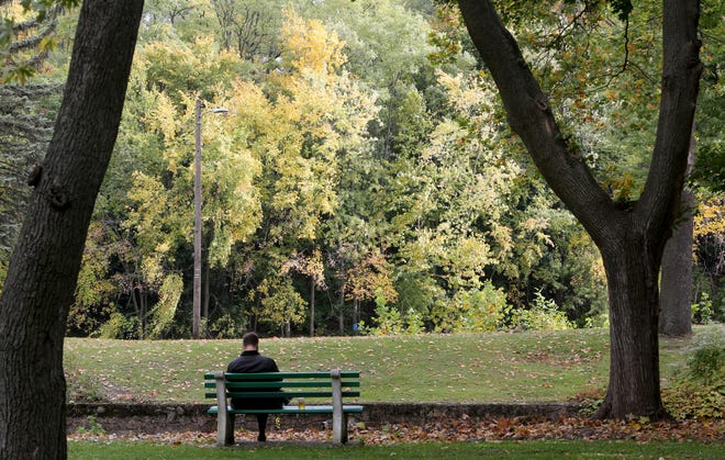 A man sits along the St. Joseph River in Leeper Park as the leaves continue their fall color show Oct. 12, 2022, in South Bend.