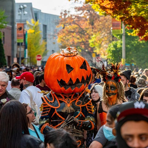 A large pumpkin-headed costumed reveller walks wit