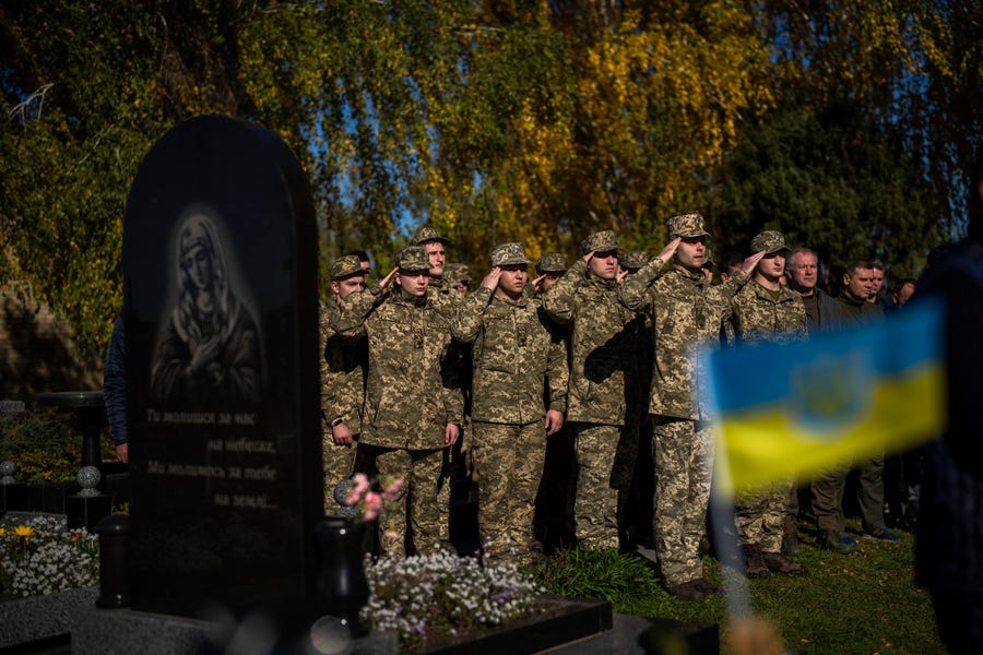 Soldiers salute as the Ukrainian national anthem is played at the funeral of Colonel Oleksiy Telizhenko in Bucha, near in Kyiv, Ukraine, Tuesday, Oct. 18, 2022.