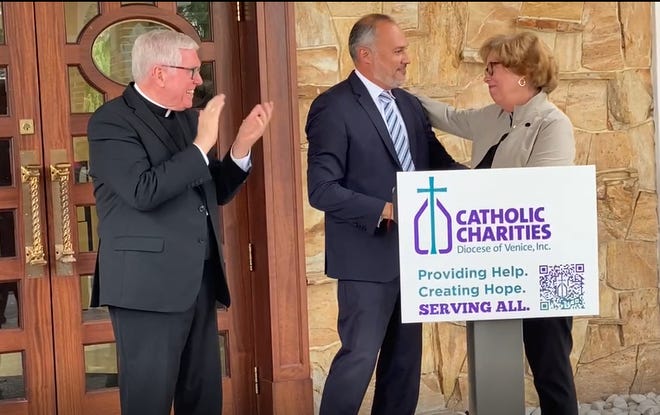 Bishop Frank J. Dewane, left, applauds as Eddie Gloria, CEO of Catholic Charities Diocese of Venice, accepts a $500,000 check from Sister Donna Markham of Catholic Charities USA to assist Hurricane Ian victims.