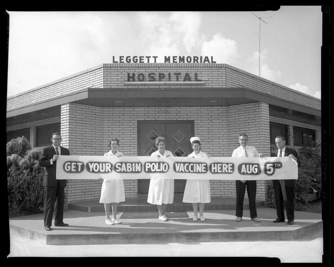 Hospital employees hold a banner in front of the Leggett Memorial Hospital announcing the arrival of the Sabin polio vaccine in Cleveland, Texas, in 1962 as photographed by Moon Young.