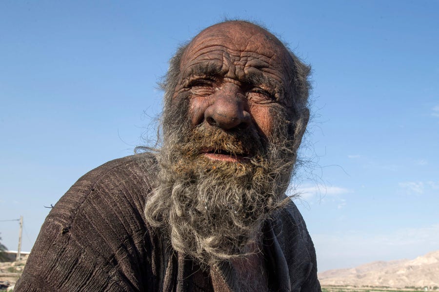 In this file photo taken on December 28, 2018 Amou Haji (uncle Haji) sits on the outskirts of the village of Dezhgah in the Dehram district of the southwestern Iranian Fars province. - An Iranian dubbed the "dirtiest man in the world" for not taking a shower for decades has died at the age of 94, state media said on October 25, 2022.