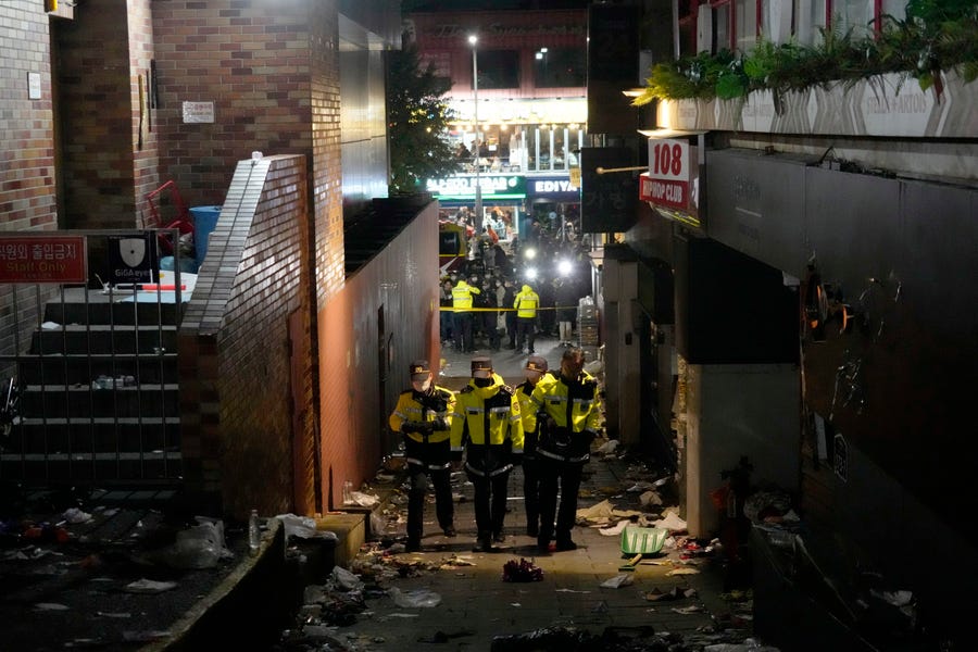 Police officers inspect the scene where people died and were injured in Seoul, South Korea, Sunday, Oct. 30, 2022, after a mass of mostly young people celebrating Halloween festivities in Seoul became trapped and crushed as the crowd surged into a narrow alley. 