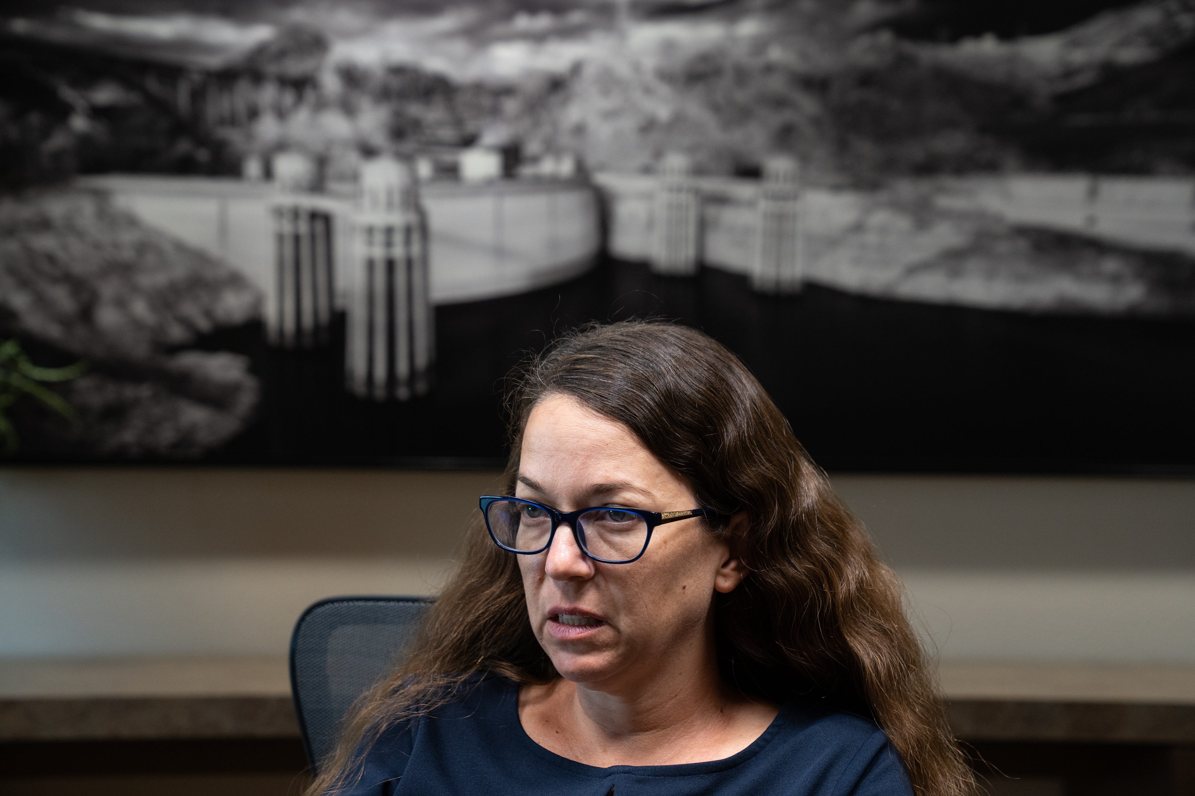 Colby Pellegrino, who has dark, wavy hair and wears glasses, sits below a picture of Hoover Dam and Lake Mead.