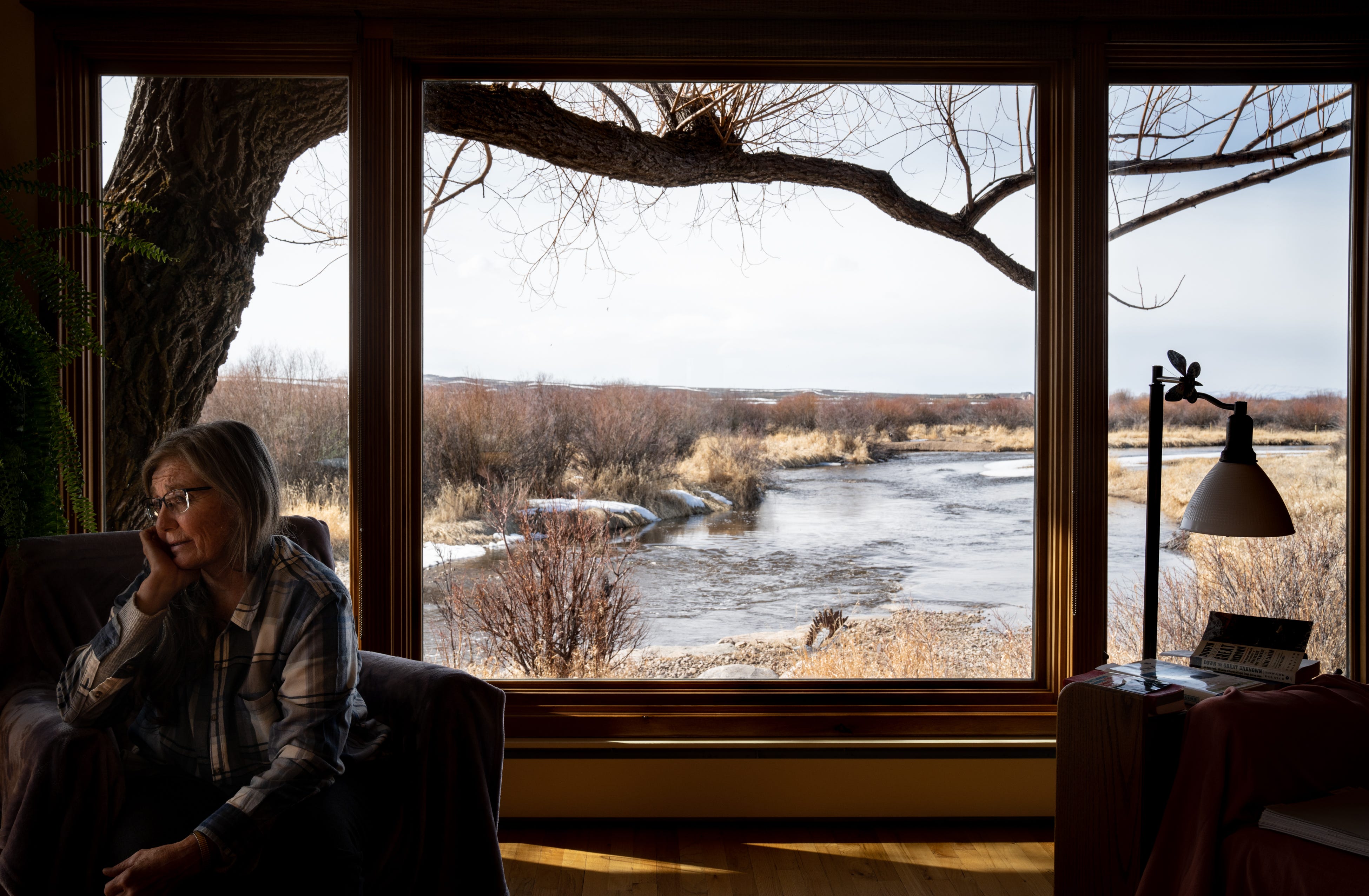 Leslie Hagenstein talks in her living room, which looks onto the New Fork River, in Pinedale, Wyoming, on March 25, 2022. Snow had receded from her lawn earlier than usual, threatening a costly repeat of the previous year’s irrigation reductions. “Last year was a real eye-opener,” she said.