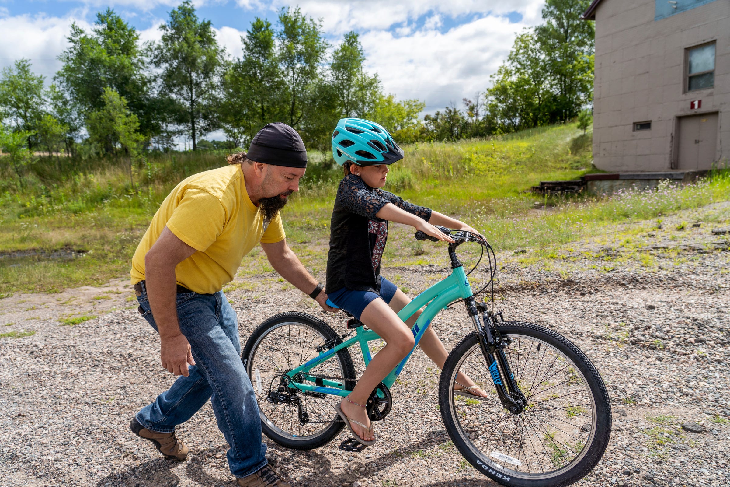 Steven Pringle, owner of Build a Bicycle - Bicycle Therapy, helps Kadence Horton, 8, of Iron River learn to ride her new bike outside of his shop in Michigan's Upper Peninsula on Friday, July 29, 2022. Pringle gave the bike and helmet to her for free after learning she and her mother had fled a domestic violence situation in New York with just the clothes on their backs.