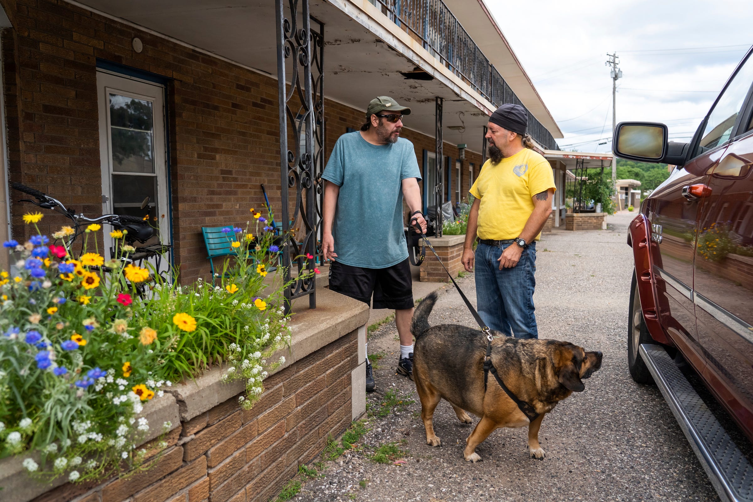Steven Pringle, right, owner of Build a Bicycle - Bicycle Therapy, stops by to talk with Army veteran Kurt Berger, 50, as he stands outside of his apartment with his dog Boone before taking his bike to tune it up back at his shop in Kingsford in Michigan's Upper Peninsula on Friday, July 29, 2022. 