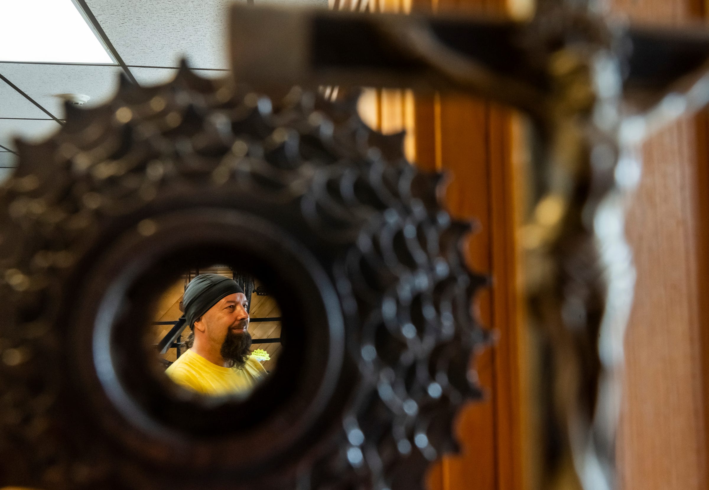 Steven Pringle, 57,owner of Build a Bicycle - Bicycle Therapy, is seen through a bicycle gear at his bike shop in Kingsford on Friday, July 29, 2022, in Michigan's Upper Peninsula.
