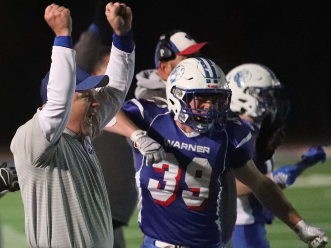 Alex Pudwill (39) and coach Jeff Gunn celebrate on the sidelines after a Warner touchdown during the Class 9A semifinal football game. Friday night in Warner. The Monarchs won 63-20 to move on to Thursday's championship game against Gregory.