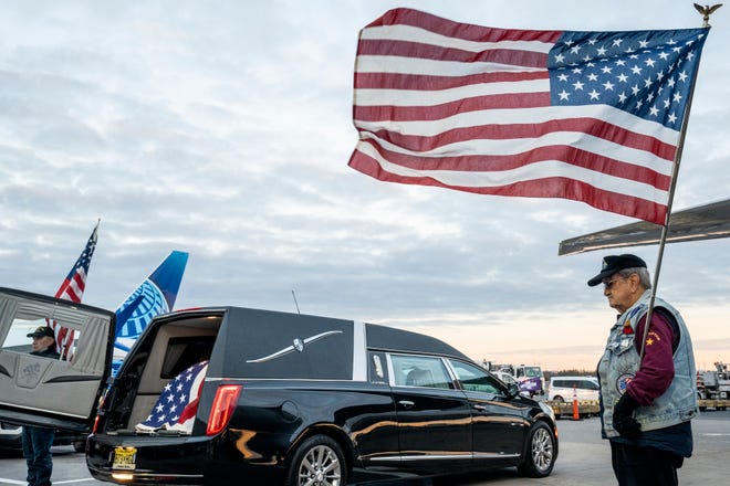 The remains of Lt. John Heffernan, a WWII American bomber navigator who was shot down in Burma in 1944, arrive at Newark Liberty Airport Tuesday, Nov. 15, 2022. Tom Greulich (left) and Jack Shinn ( fight) with the Patriot Guard Riders hold flags near the hearse containing Heffernan's casket.