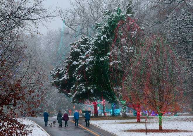 A light snowfall combines with lights for the upcoming 'Winter Wonderland' at Tilles Park in Ladue, Mo., as part of a women's dog walking group makes their way through the street on Tuesday.