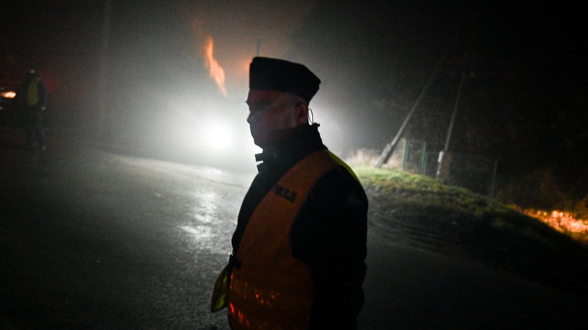 A police officer walks past a check point as permitted cars are allowed to cross into the crime scene on November 16, 2022 in Przewodow, Poland. Poland convened a meeting of its national security council amid reports that stray missiles hit its territory, killing two people. Russia's defense ministry denied that its missiles hit the NATO member state, but moments after, Polish ministry confirmed it was a Russian-produced missile.