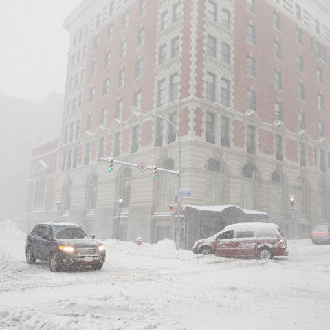 Cars drive along Ellicott Street as snow falls Fri