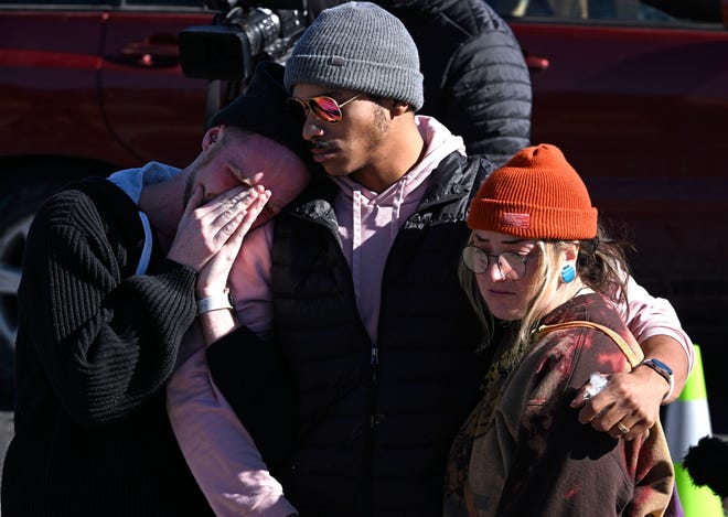 Tyler Johnston, left, his fiance Keenan Mestas-Holmes, center, and their friend Atlas Precious hug each other as they pay their respects Sunday at a makeshift memorial near Club Q in Colorado Springs, Colorado.