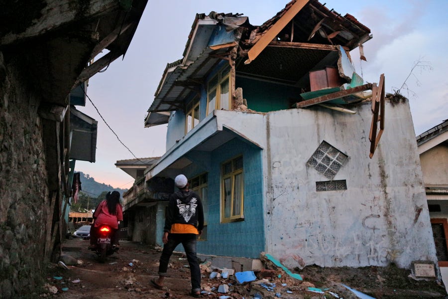 A man walks past a house damaged by an earthquake in Cianjur, West Java, Indonesia, Monday, Nov. 21, 2022. The strong, shallow earthquake toppled buildings and collapsed walls on Indonesia's densely populated main island of Java on Monday, killing a number of people and injuring hundreds as people rushed into the streets, some covered in blood and white debris.