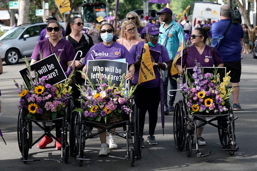 Nursing home workers, home care workers and supporters march through the streets pushing flower covered hospital beds and wheelchairs as they block traffic in downtown Sacramento, Calif., in June 2022. The march was held to bring attention to what they call is the workforce crisis that has left nursing homes understaffed, workers disabled and compromised the care for elderly and disabled residents.
