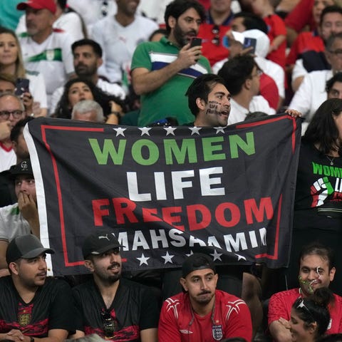 An Iranian fan holds up a banner reading "Women Li