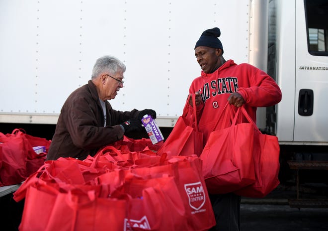 Volunteers Henry Aegerter, left, and Fred Haywood prepare to load bags of groceries into vehicles Tuesday morning during the annual SAM Center Thanksgiving food giveaway, which benefits local U.S. military members, families and veterans. More than 500 were expected to receive food during the event in Massillon.