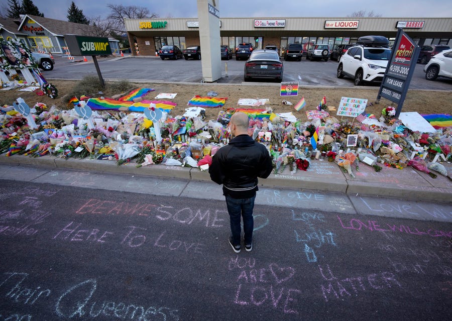 A lone mourner stands amid chalk messages and a makeshift memorial for the victims of a mass shooting at Club Q, a popular LGBTQ club in Colorado Springs.