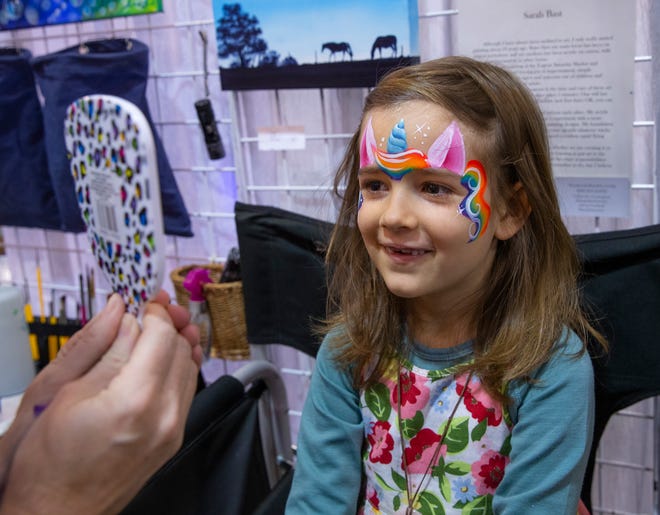 Six-year-old Sati Kryl gets a first look at her new unicorn face paint created by artist Sarah Bast at her booth Poppinfrizzle during the Holiday Market at the Lane Event Center in Eugene Saturday.