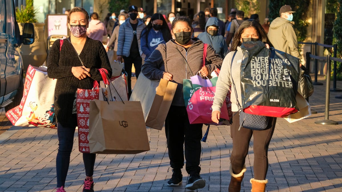 Black Friday shoppers wearing face masks carry bags at the Citadel Outlets in Commerce, Calif., Friday, Nov. 26, 2021. The National Retail Federation, the nation's largest retail trade group, expects that holiday sales growth this year will slow to a range of 6% to 8%, compared to 13.5% a year ago. The trade group said Thursday, Nov. 3, 2022,  that it predicts that sales for the November and December period will grow to between $942.6 billion to $960.4   billion.