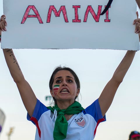 A woman holds up a sign reading Mahsa Amini, the n