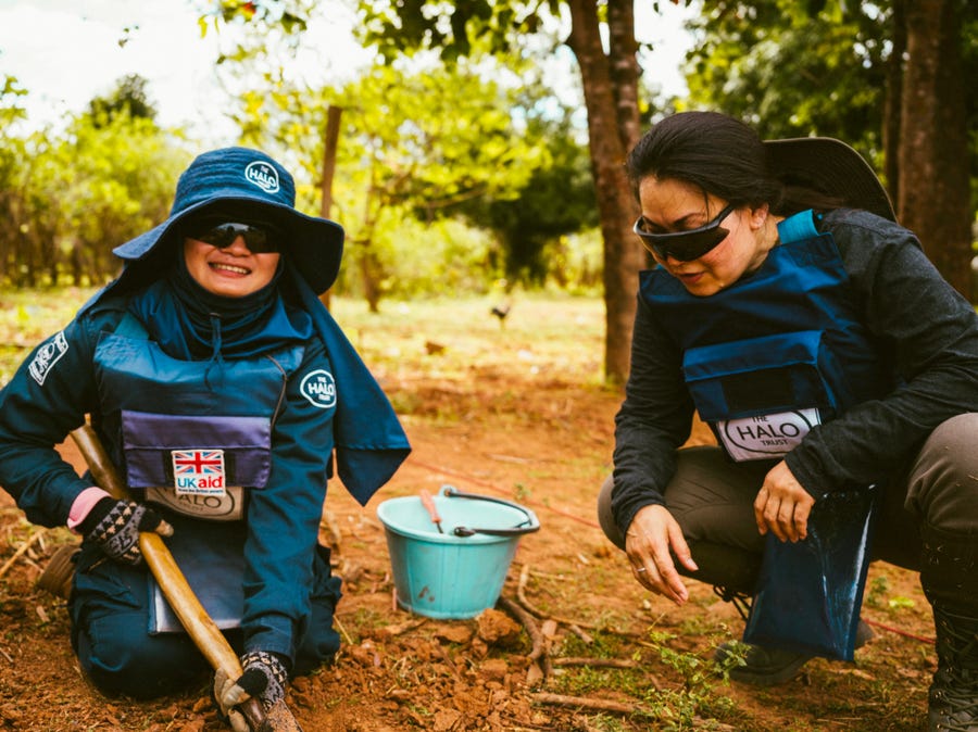 Khamsone Sirimanivong, right, learns from a HALO Trust deminer in southern Laos on Nov. 9, 2022. The 21-year-old deminer is digging up bomb fragments found by a metal detector.