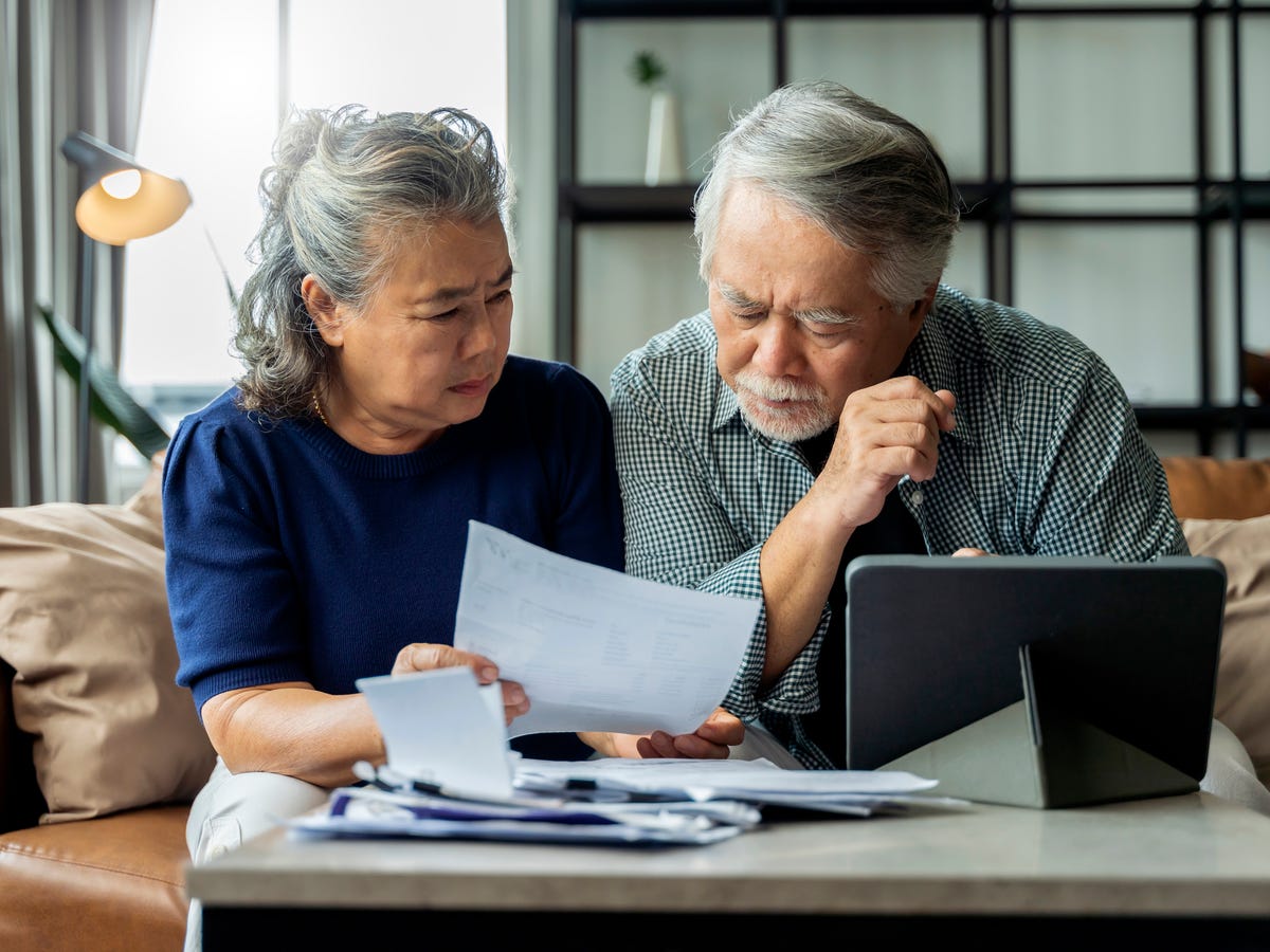 Old Retired Asian Senior Couple Checking And Calculate Financial Billing Together On Sofa Involved In Financial Paperwork Paying Taxes Online Using E Banking Laptop At Living Room Home Background