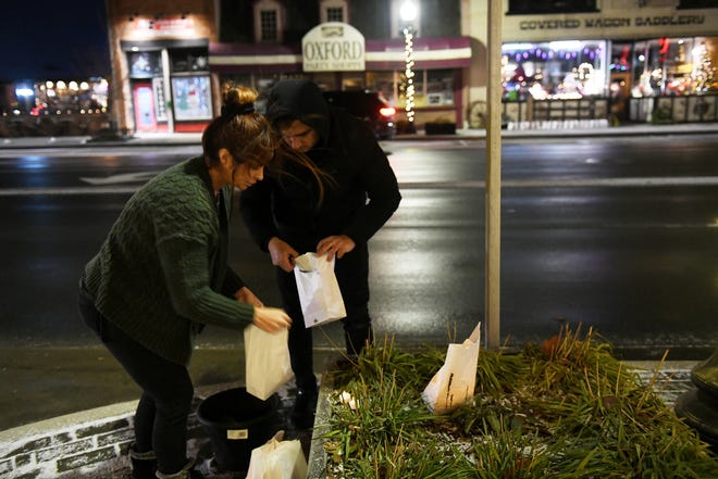 Dari kiri, Marcela Chisaca dari Auburn Hills dan manajer di restoran Casa Real dan Diego Fajardo meletakkan tanah di dasar luminari yang dikantongi untuk diletakkan di depan restoran di Oxford pada 30 November 2022. Tokoh-tokoh terkenal dinyalakan dan dipajang di Oxford untuk mengenang empat siswa yang terbunuh satu tahun lalu di Oxford High School.