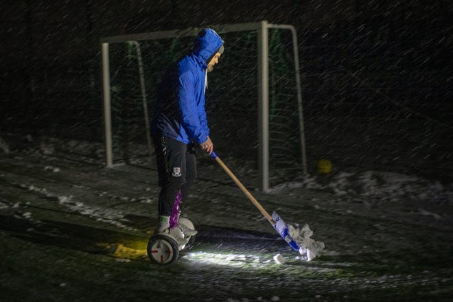 Een man rijdt op zijn hoverboard terwijl hij sneeuw ruimt van een veld voor een voetbalwedstrijd in Irpin, regio Kiev, Oekraïne, dinsdag 29 november 2022.