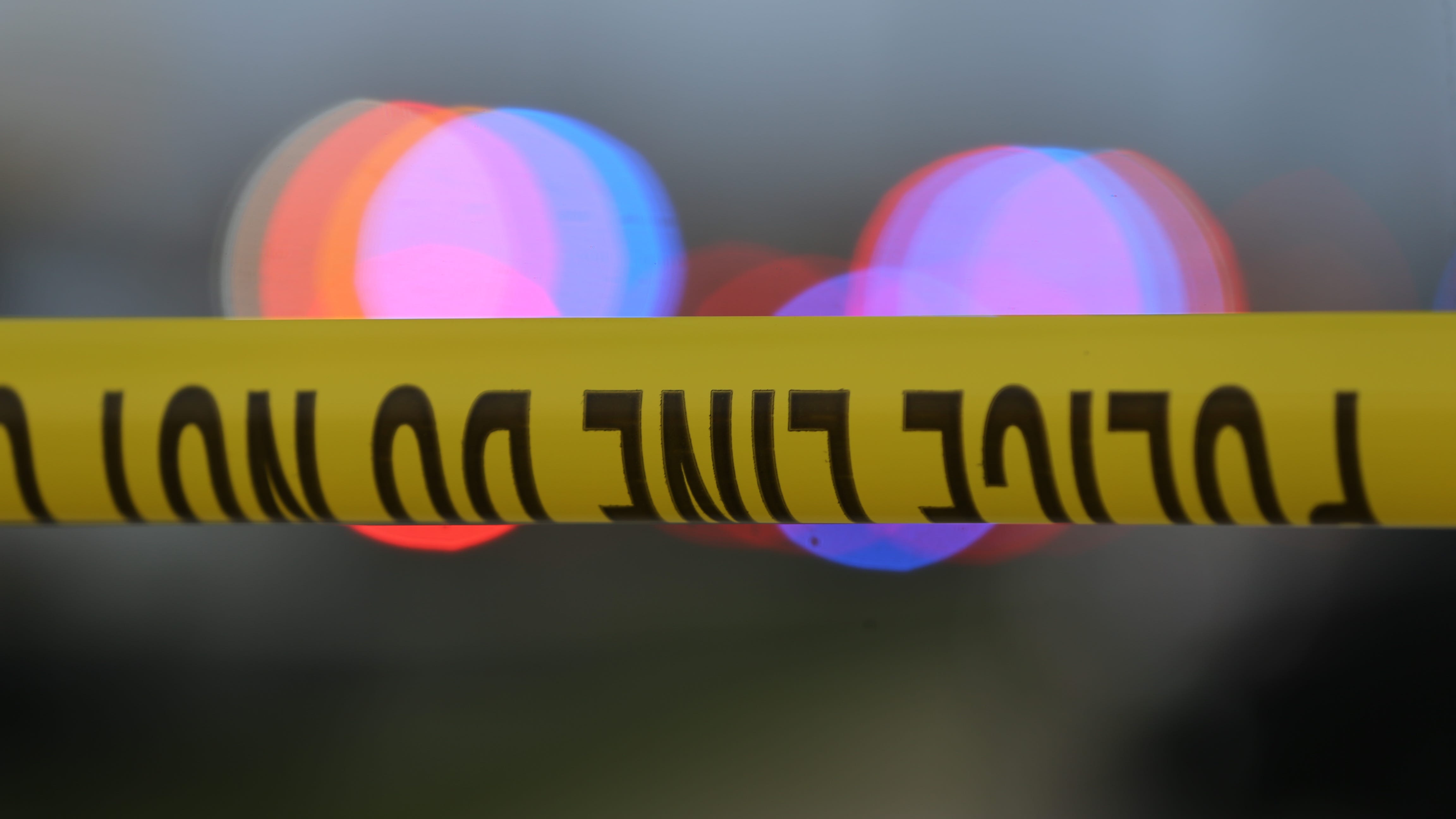 Police tape is strung up with police sirens flashing in the background.
