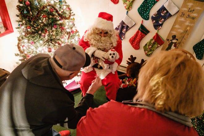 Terry Tenger, left, signals the family dog, Daisy, a poodle-Pomeranian mix, as his wife Tara takes pictures of Santa next to Dover City Hall. Interim Mayor Shane Gunnoe, who is portraying Santa this year, said, "This is the first time we've done this since COVID."