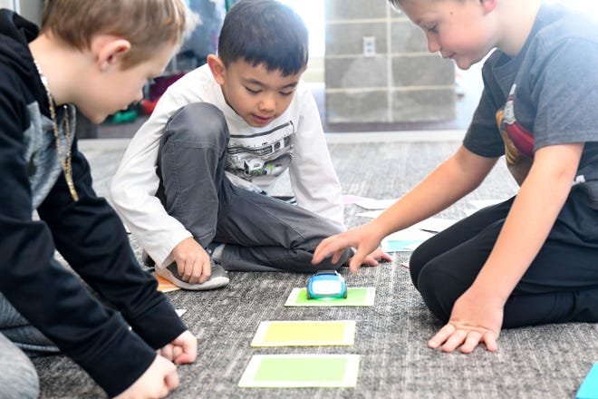 First graders Sawyer Amolins, Silas Koutserath and Declan Angelo learn the beginnings of coding by sequencing colored tiles for driving robots on Thursday, December 8, 2022, at Adventure Elementary in Harrisburg.