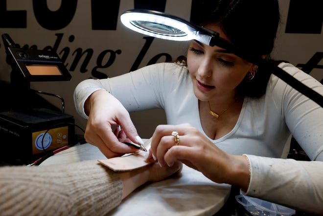 Zainab Sobh, de 25 años, de Canton y propietaria de Ayla's Links, coloca joyas permanentes en un cliente durante su ubicación emergente en The Flower Shop Detroit en Dearborn Heights el 9 de diciembre de 2022. Coffee Shop in One abrió en octubre de 2022.