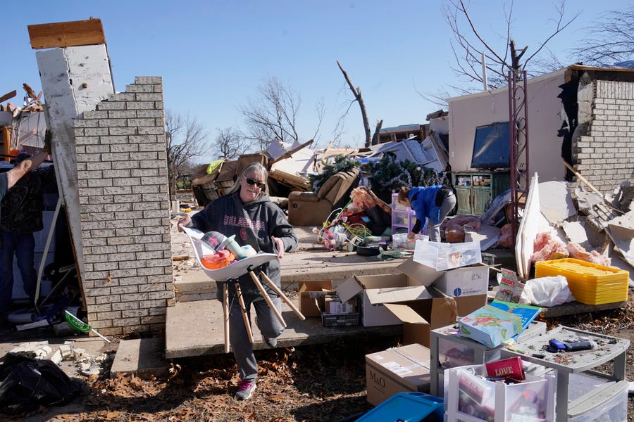 Belinda Penner carries belongings from her cousin's home, destroyed by a tornado on Tuesday, Dec. 13, 2022, in Wayne, Okla.